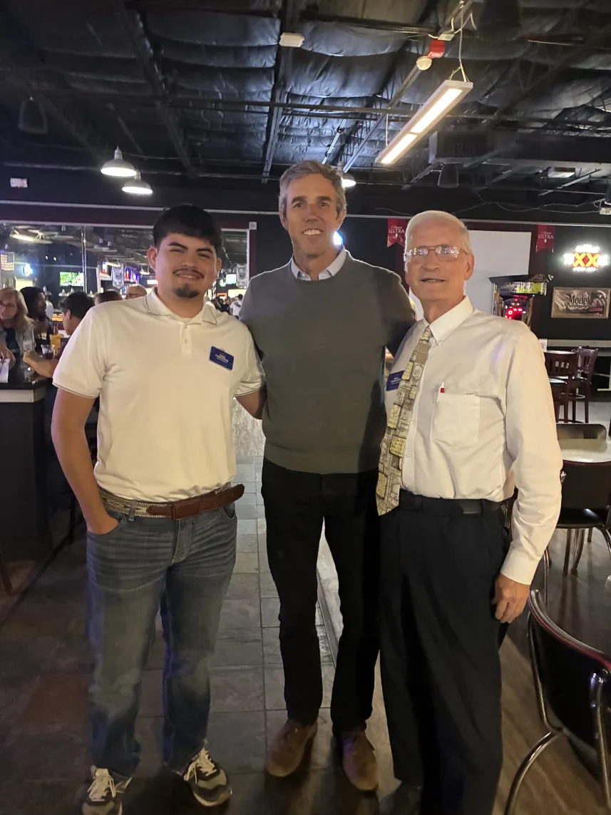 Three men standing together in a dimly lit indoor setting.