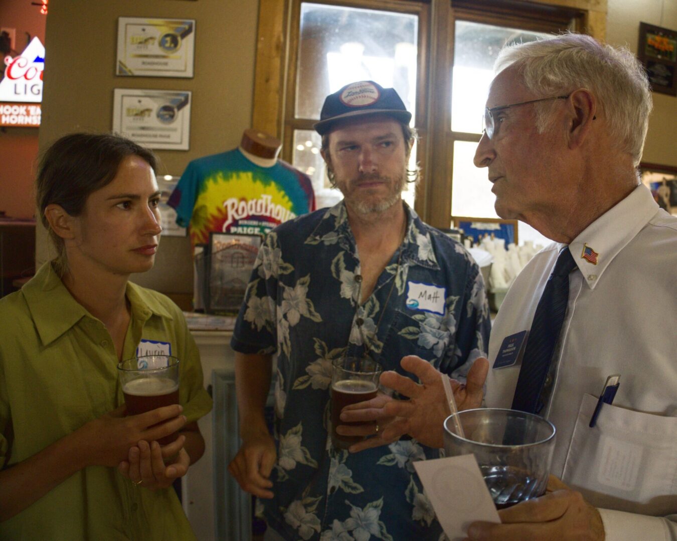 Three people talking in bar holding beers